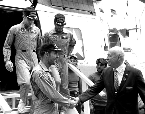 Dr. Robert R. Gilruth, director of the Manned Spacecraft Center greets Apollo 15 Mission Commander David R. Scott as he and astronauts Alfred M. Worden (Command Module Pilot), center and James B. Irwin (lunar module pilot) leave the recovery helicopter aboard the USS Okinawa after a successful splashdown on August 7, 1971